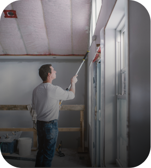 Peintre en train de travailler sur les finitions d’un mur à l’intérieur d’un bâtiment rénové, symbolisant une attention aux détails.