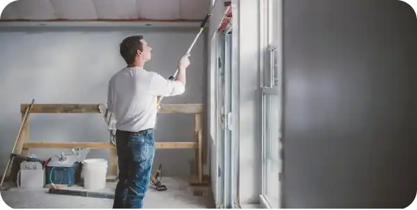 Peintre en train de travailler sur les finitions d’un mur à l’intérieur d’un bâtiment rénové, symbolisant une attention aux détails.