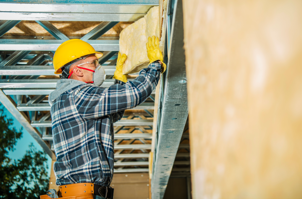Artisan installant de la laine isolante dans une structure métallique, illustrant un travail conforme aux normes de construction modernes.