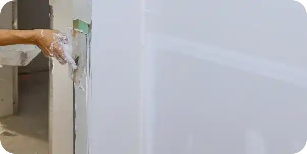 Main appliquant de l’enduit sur un mur lisse, illustrant la phase finale de préparation avant peinture.